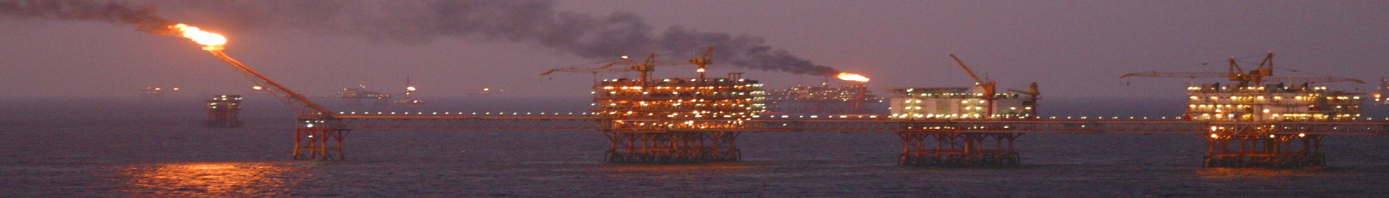 Offshore oil platform at night, with a lit gas flare and smoke from the process towers